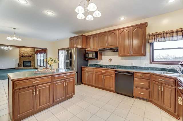 kitchen featuring under cabinet range hood, hanging light fixtures, black appliances, brown cabinetry, and dark countertops