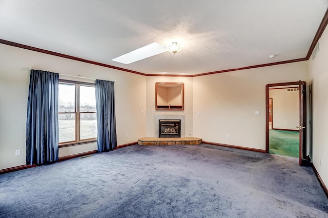 unfurnished living room with a skylight, ornamental molding, carpet flooring, a tile fireplace, and baseboards