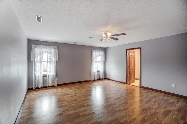 unfurnished room with baseboards, visible vents, ceiling fan, wood finished floors, and a textured ceiling