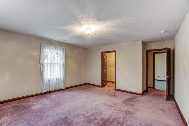 unfurnished room featuring baseboards, a textured ceiling, and light colored carpet