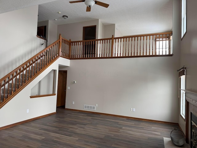 unfurnished living room featuring dark wood-style floors, a glass covered fireplace, a towering ceiling, and visible vents