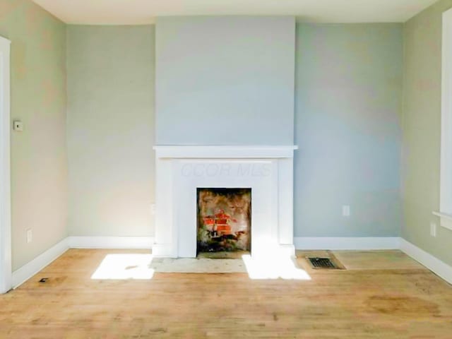 unfurnished living room featuring wood finished floors, a fireplace with flush hearth, visible vents, and baseboards