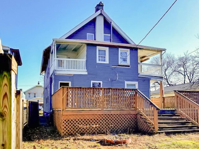 back of house featuring a balcony, a chimney, and a wooden deck