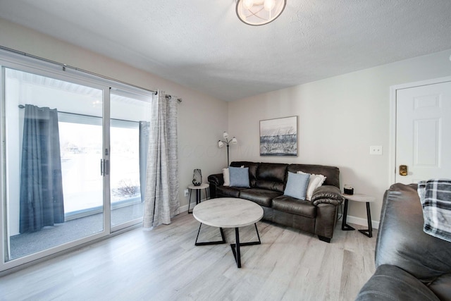 living room featuring a textured ceiling, light wood-type flooring, and baseboards