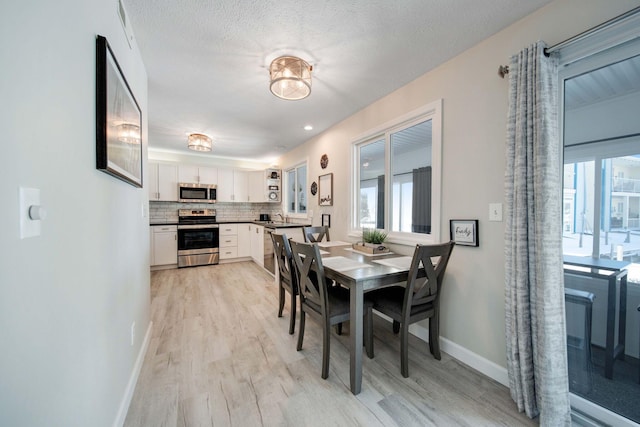 dining room with light wood-type flooring, a healthy amount of sunlight, a textured ceiling, and baseboards