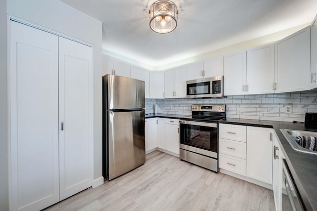 kitchen featuring stainless steel appliances, dark countertops, white cabinets, and light wood-style floors