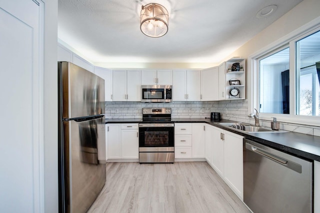 kitchen with dark countertops, stainless steel appliances, white cabinetry, open shelves, and a sink