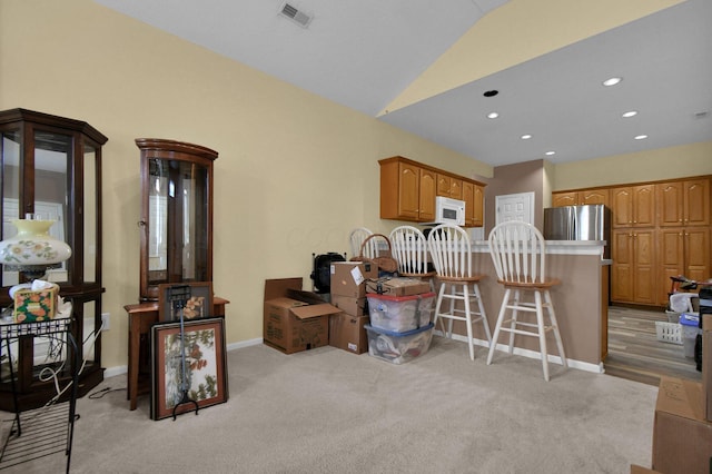 kitchen with lofted ceiling, visible vents, a kitchen breakfast bar, freestanding refrigerator, and brown cabinetry