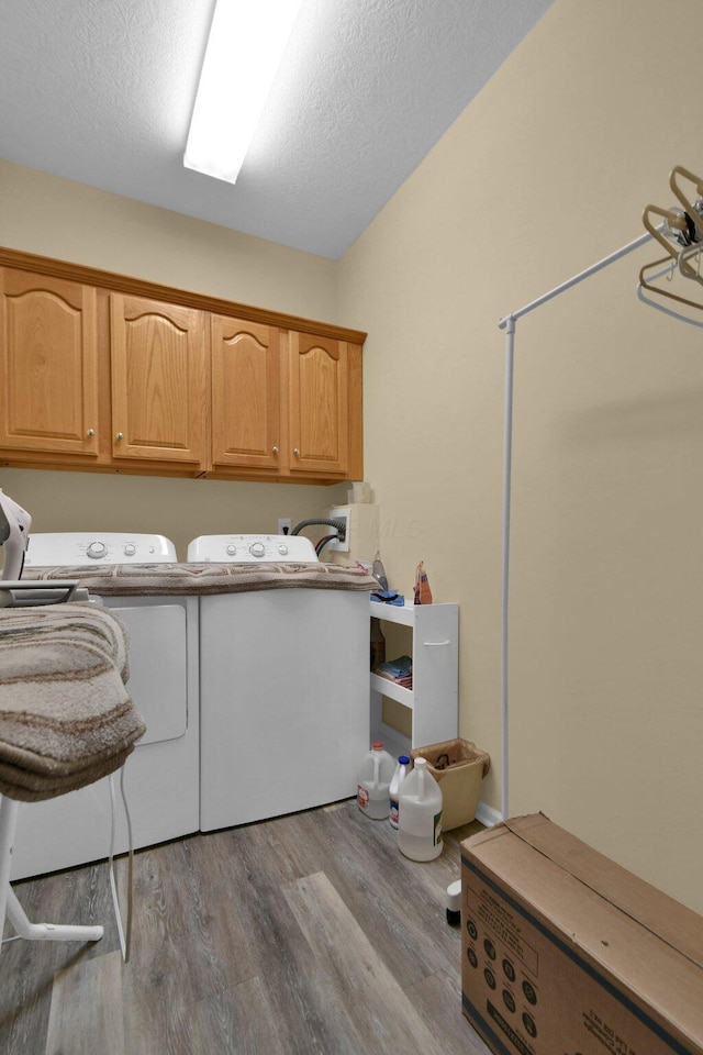 washroom with washing machine and dryer, cabinet space, a textured ceiling, and light wood finished floors