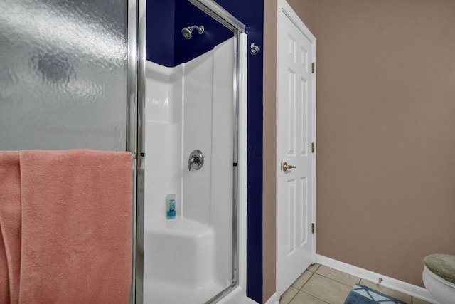 bathroom with toilet, a shower stall, baseboards, and tile patterned floors