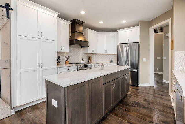 kitchen featuring a barn door, stainless steel appliances, white cabinets, backsplash, and custom range hood