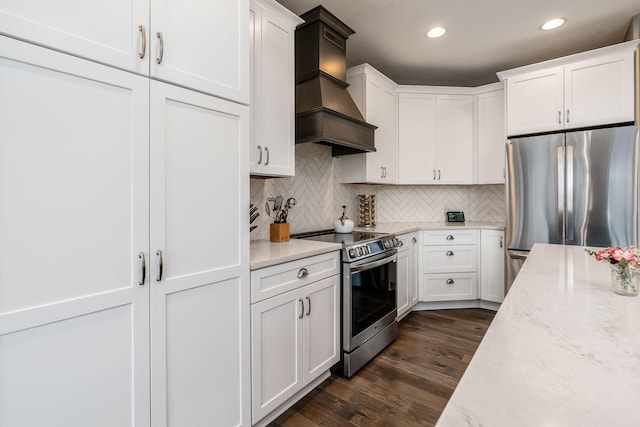 kitchen with dark wood finished floors, decorative backsplash, appliances with stainless steel finishes, premium range hood, and white cabinetry