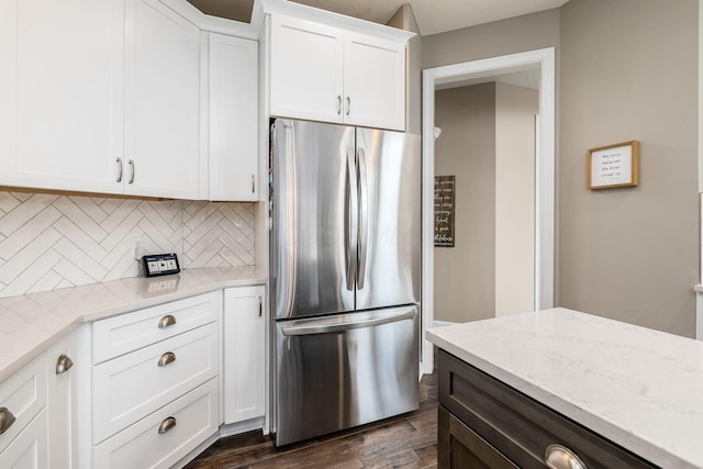 kitchen featuring dark wood-style floors, backsplash, freestanding refrigerator, white cabinetry, and light stone countertops