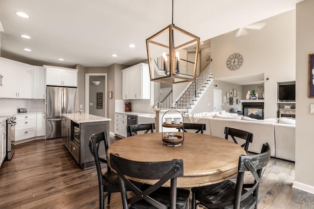 dining space featuring an inviting chandelier, stairs, dark wood finished floors, and a glass covered fireplace