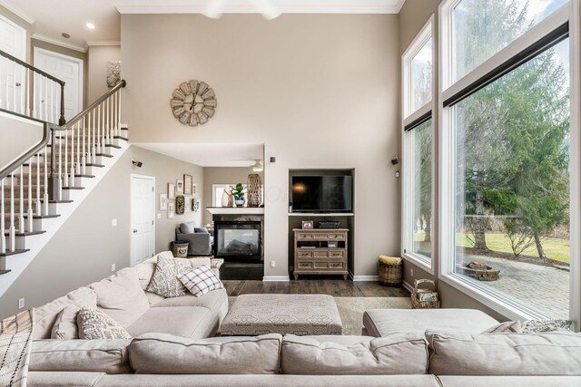 living area featuring wood finished floors, a glass covered fireplace, a high ceiling, and crown molding