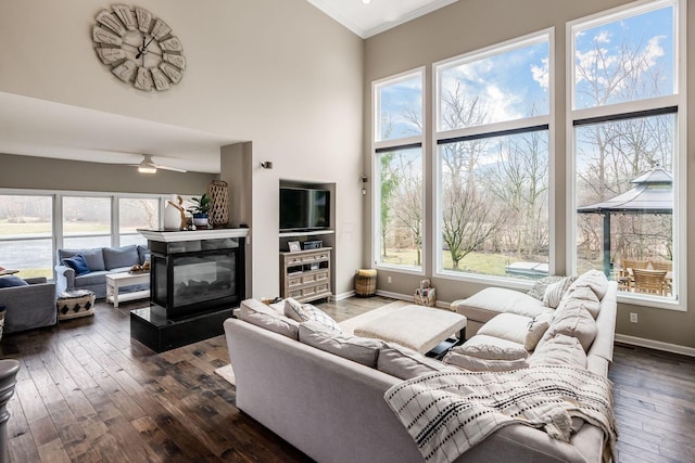 living room featuring dark wood-style floors, ornamental molding, a towering ceiling, and baseboards