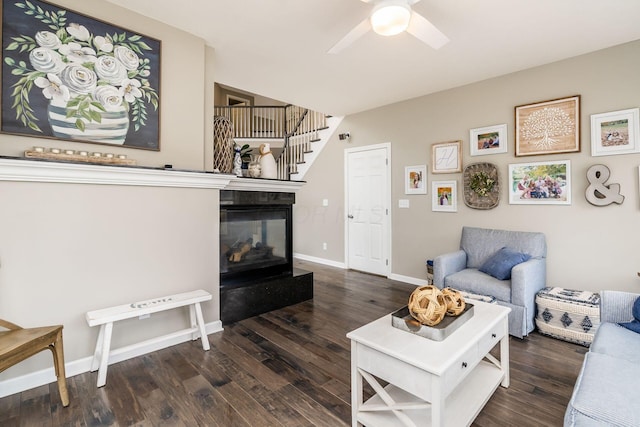 living area featuring a ceiling fan, baseboards, wood finished floors, and a multi sided fireplace