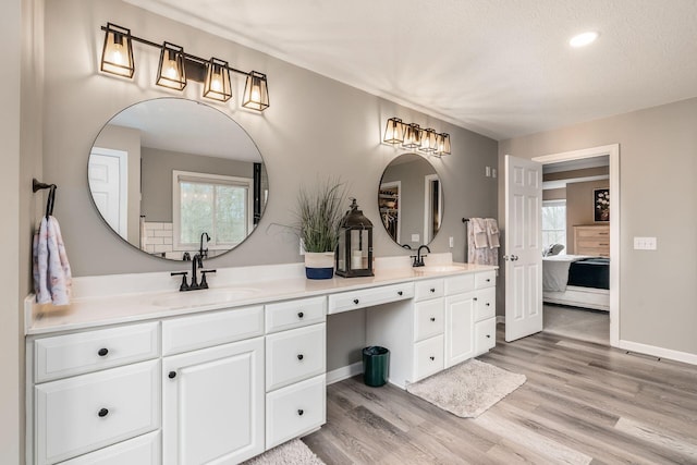 ensuite bathroom featuring wood finished floors, a sink, ensuite bath, and double vanity