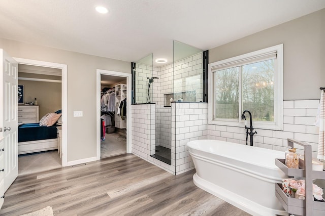 bathroom with tile walls, a freestanding bath, connected bathroom, wood finished floors, and a walk in shower