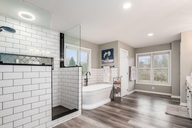 full bath featuring wood finished floors, a textured ceiling, a freestanding bath, a healthy amount of sunlight, and a walk in shower