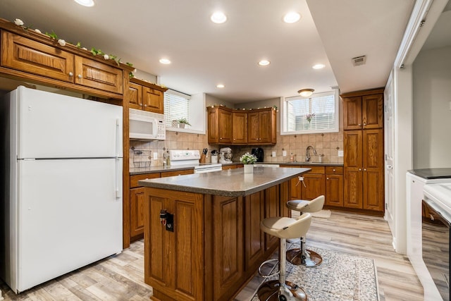 kitchen featuring visible vents, brown cabinetry, a sink, a kitchen island, and white appliances