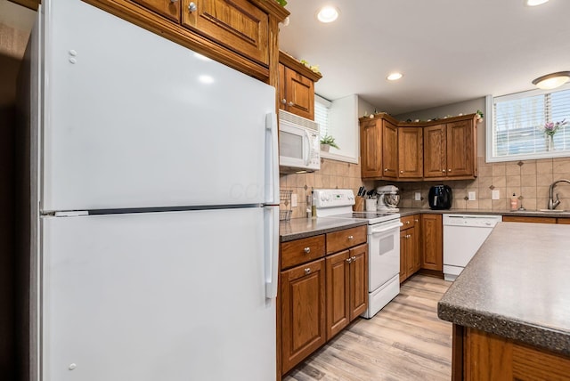 kitchen featuring white appliances, brown cabinetry, dark countertops, and a sink