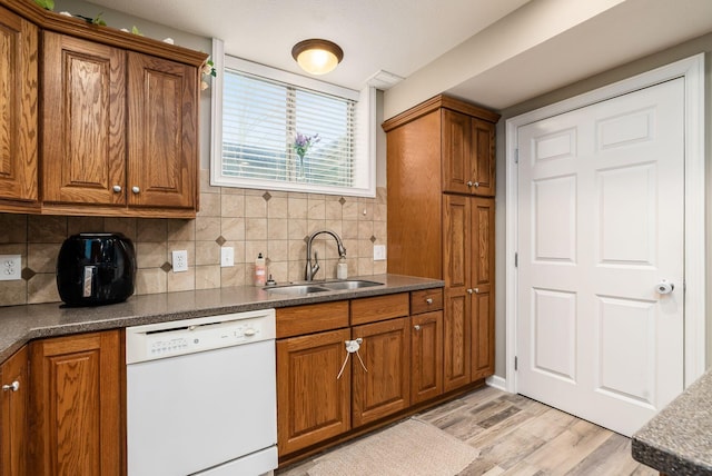 kitchen featuring tasteful backsplash, dark countertops, brown cabinets, white dishwasher, and a sink