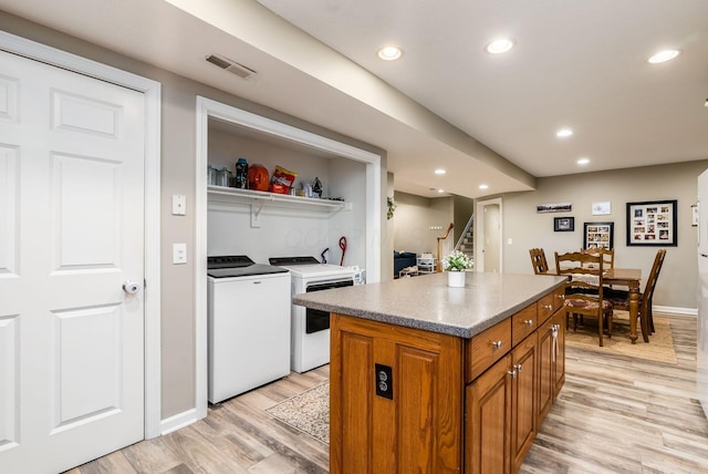 kitchen with a center island, brown cabinets, washer and clothes dryer, visible vents, and light wood-style flooring