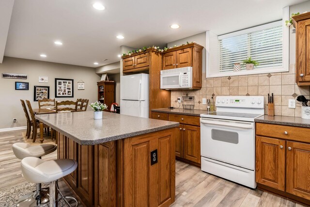 kitchen featuring tasteful backsplash, white appliances, a kitchen bar, and brown cabinets