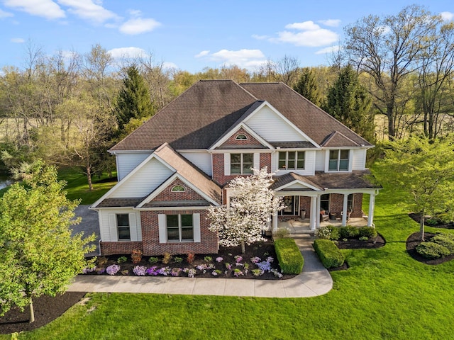 craftsman inspired home featuring roof with shingles, covered porch, a front lawn, and brick siding
