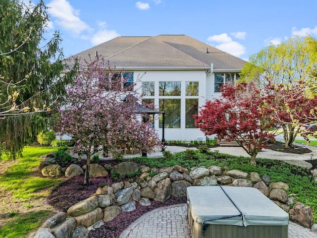 view of side of home featuring a shingled roof and a hot tub