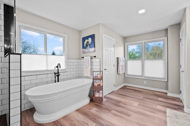 bathroom with recessed lighting, a freestanding tub, tile walls, and wood finished floors