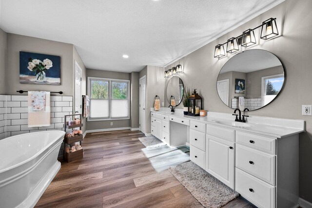 bathroom with a freestanding bath, a sink, double vanity, recessed lighting, and wood finished floors