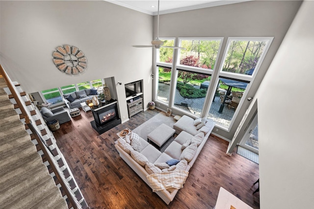 living area featuring ornamental molding, wood finished floors, a fireplace, ceiling fan, and a high ceiling