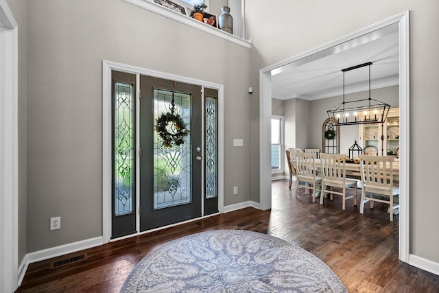 entrance foyer featuring visible vents, ornamental molding, wood finished floors, and a chandelier