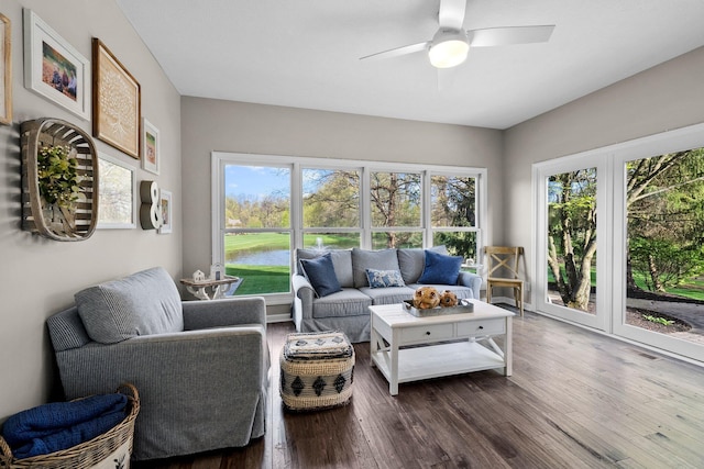 living area featuring a ceiling fan, dark wood-style flooring, a water view, and a healthy amount of sunlight