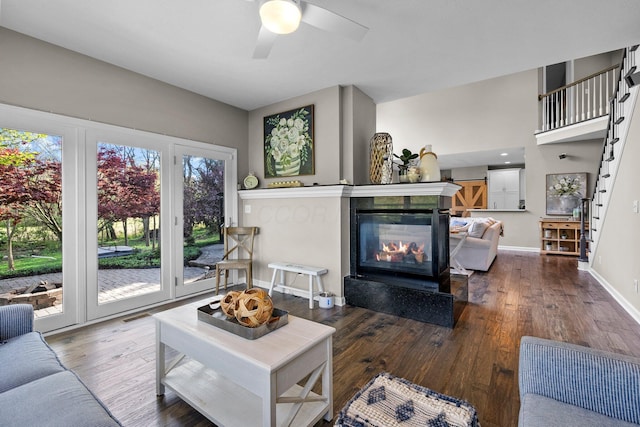 living area with a multi sided fireplace, baseboards, a ceiling fan, and wood finished floors