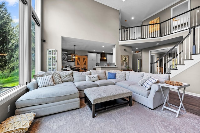 living room with a towering ceiling, crown molding, wood finished floors, stairway, and baseboards