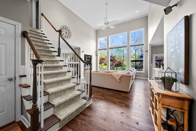 interior space featuring a ceiling fan, crown molding, wood finished floors, baseboards, and a high ceiling