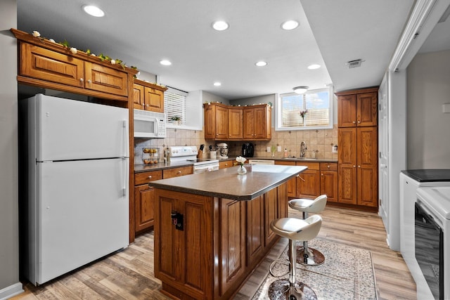 kitchen featuring light wood-style floors, brown cabinets, white appliances, and a center island