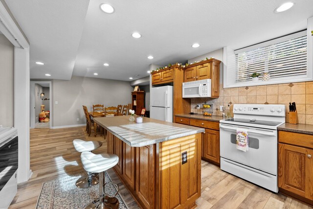 kitchen featuring a center island, tasteful backsplash, brown cabinetry, and white appliances