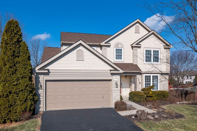 traditional-style house with a shingled roof, stone siding, aphalt driveway, an attached garage, and fence