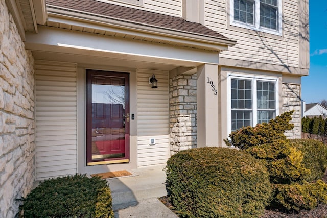 doorway to property featuring stone siding and a shingled roof