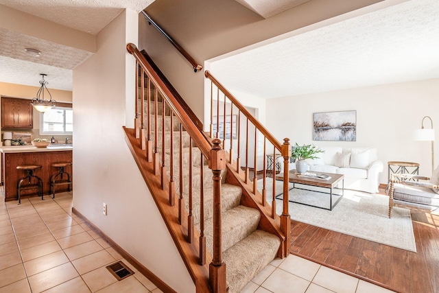 stairway featuring a textured ceiling, baseboards, visible vents, and tile patterned floors