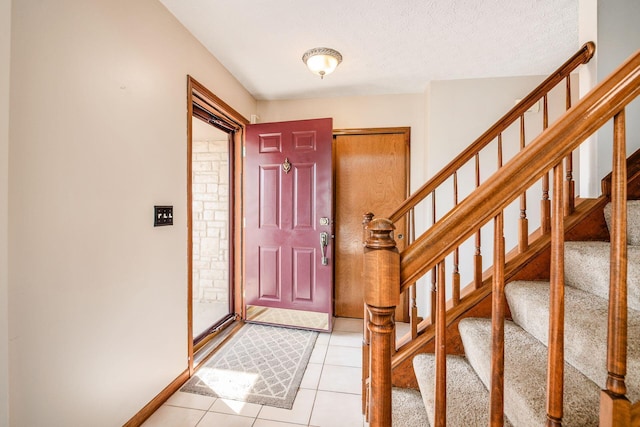 foyer entrance with light tile patterned flooring, a textured ceiling, baseboards, and stairs