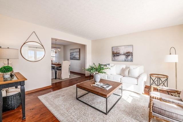 living area featuring a notable chandelier, a textured ceiling, baseboards, and wood finished floors