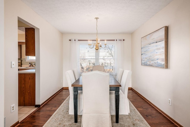 dining space featuring a textured ceiling, baseboards, dark wood finished floors, and an inviting chandelier