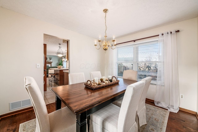 dining space with a chandelier, a textured ceiling, wood finished floors, visible vents, and baseboards