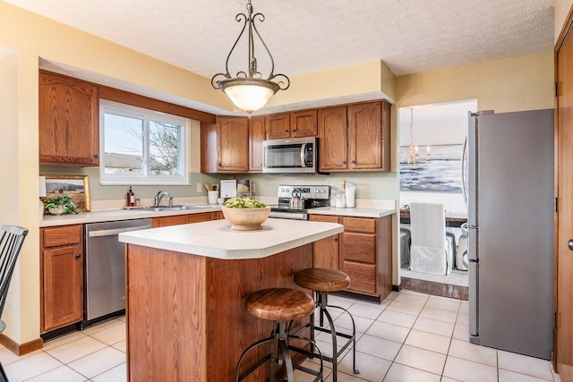 kitchen with appliances with stainless steel finishes, brown cabinets, a center island, light countertops, and a sink