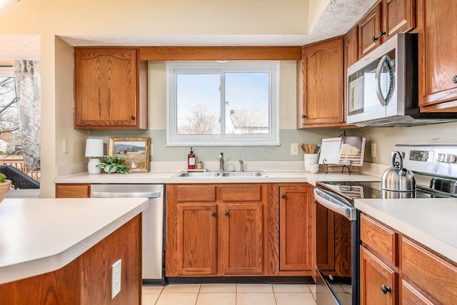 kitchen with brown cabinetry, stainless steel appliances, a sink, and light countertops